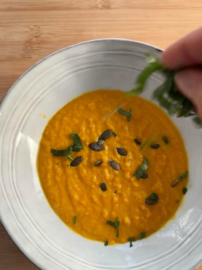 Une assiette de soupe aux carottes, parsemée de coriandre